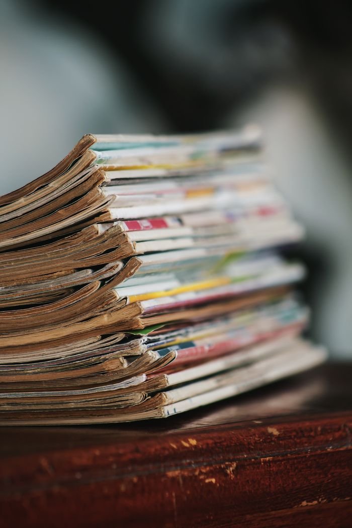 Close-up of a stack of worn magazines on a wooden table with a blurred background.