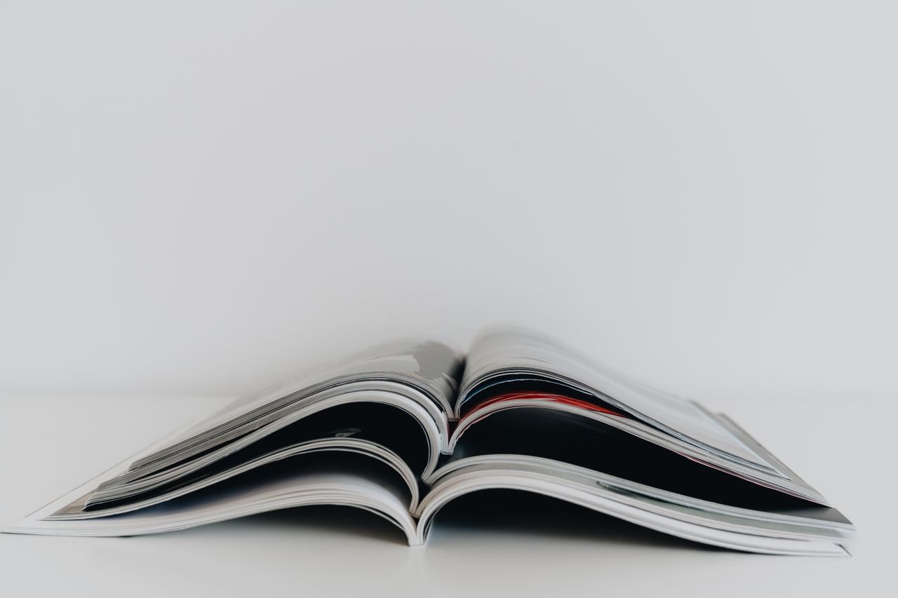 Minimalist image of an open magazine on a white table, ideal for literature topics.
